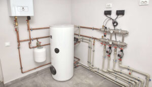 White cylindrical water heater tank with copper and stainless steel piping, valves, and electronic controls in a utility room.