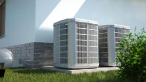 Multiple gray and white residential air conditioning units installed on a concrete pad beside a modern home with landscaping.