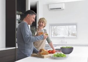 Mature couple smiling while preparing food in a modern kitchen with an air conditioning unit visible on the wall.