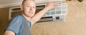 Technician in blue shirt installing or replacing an air conditioning filter in a ceiling-mounted HVAC unit.