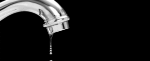 Chrome faucet with water dripping from the spout against a black background.