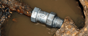 Metal pipe coupling submerged in muddy water during underground plumbing installation or repair work.