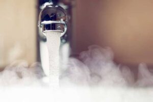 Close-up of a faucet aerator dispensing hot water with visible steam and vapor rising from the spout.