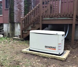 White Generac standby generator unit mounted on concrete pad beside brown wooden deck stairs and red brick house foundation.
