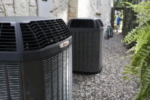 Multiple black outdoor air conditioning and heating units installed on gravel beside a residential home with stone exterior.