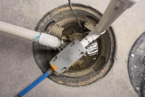 Sump pump system installed in basement sump pit with white PVC pipe, blue discharge line, and electrical cord connections.