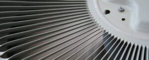 Close-up view of an air conditioner fan with metal fins and white housing showing ventilation details.