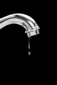 Chrome faucet with water dripping downward against a black background, illustrating a plumbing leak issue.