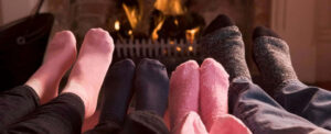 Multiple people wearing cozy socks warming their feet by a fireplace. Warm, comfortable home heating scene.