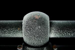 A metal pipe covered in thick white frost and ice crystals against a dark background, illustrating frozen plumbing conditions.