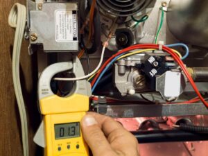Technician using yellow clamp meter to measure 0.13 amperage on furnace heating system during maintenance inspection.