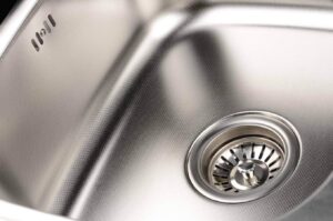 Close-up of a polished stainless steel kitchen sink basin with a chrome drain strainer basket visible.