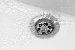 Overhead view of a circular water drain surrounded by white surface with textured patterns and dark drainage openings.