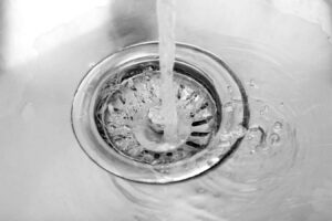 Water streams down through a circular drain hole with splashing water and bubbles visible around the metal drain cover.