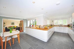 Spacious modern kitchen with white cabinetry, wood countertops, and dark tile flooring opens to dining and living areas.