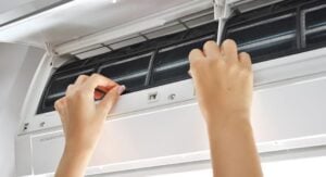 Hands removing a red air filter from an indoor HVAC unit during routine maintenance.