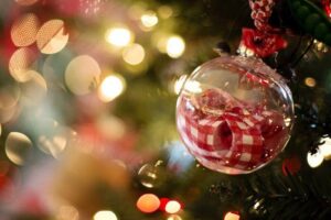 Clear glass Christmas ornament with red and white plaid pattern hanging on evergreen tree with warm bokeh lights in background.